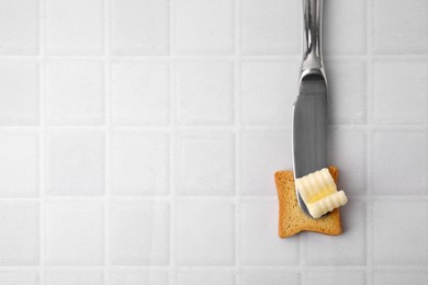 Tasty butter curl, knife and piece of dry bread on white tiled table, top view. Space for text