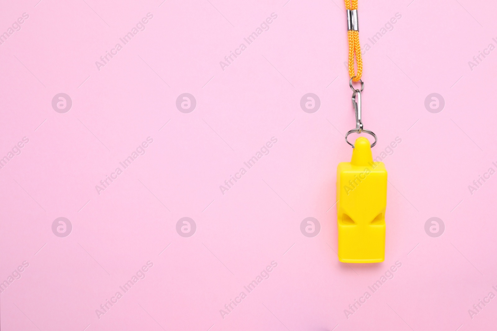 Photo of One yellow whistle with orange cord on pink background, top view. Space for text