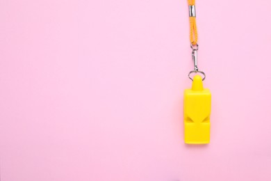 Photo of One yellow whistle with orange cord on pink background, top view. Space for text