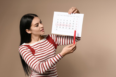 Photo of Young woman holding calendar with marked menstrual cycle days on beige background