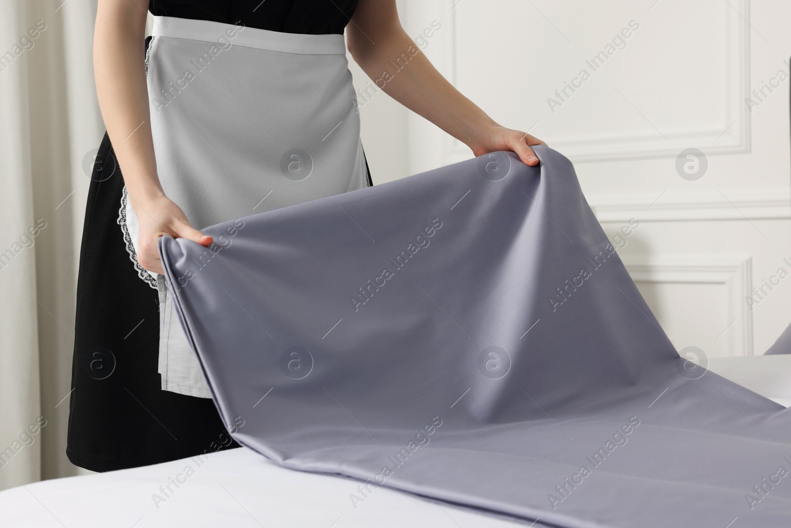 Photo of Young maid making bed in hotel room, closeup