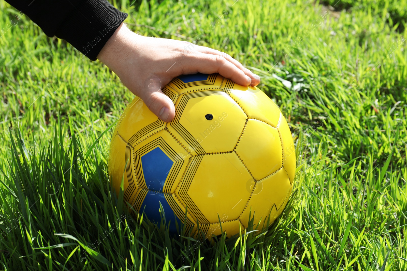 Photo of Man holding yellow soccer ball on green grass, closeup