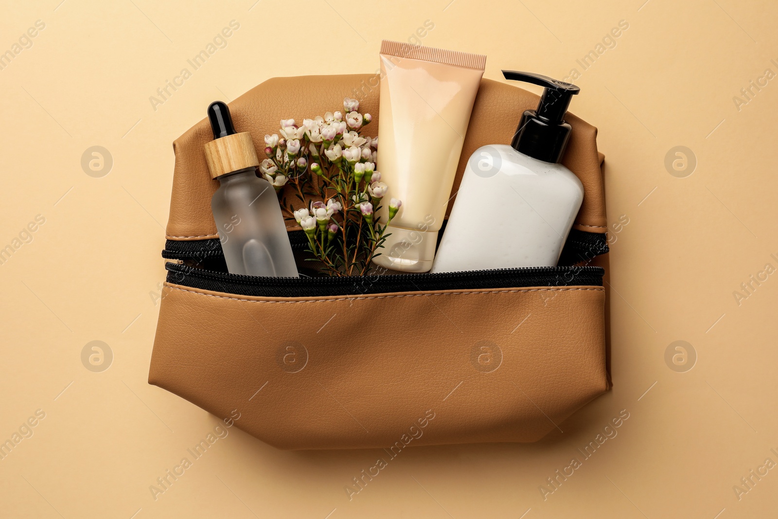 Photo of Preparation for spa. Compact toiletry bag with different cosmetic products and flowers on light brown background, top view