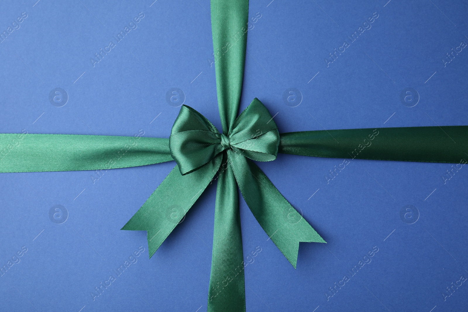 Photo of Green satin ribbon with bow on blue background, top view