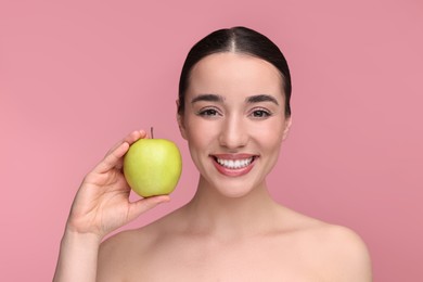 Beautiful young woman with apple on pink background