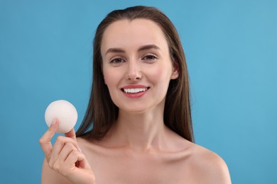Happy young woman holding face sponge on light blue background