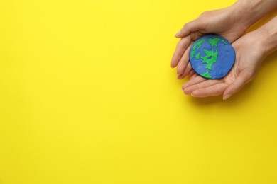 Photo of Woman holding plasticine model of planet on yellow background, top view with space for text. Earth Day