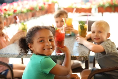 Photo of Cute children with glasses of natural lemonades at table in cafe