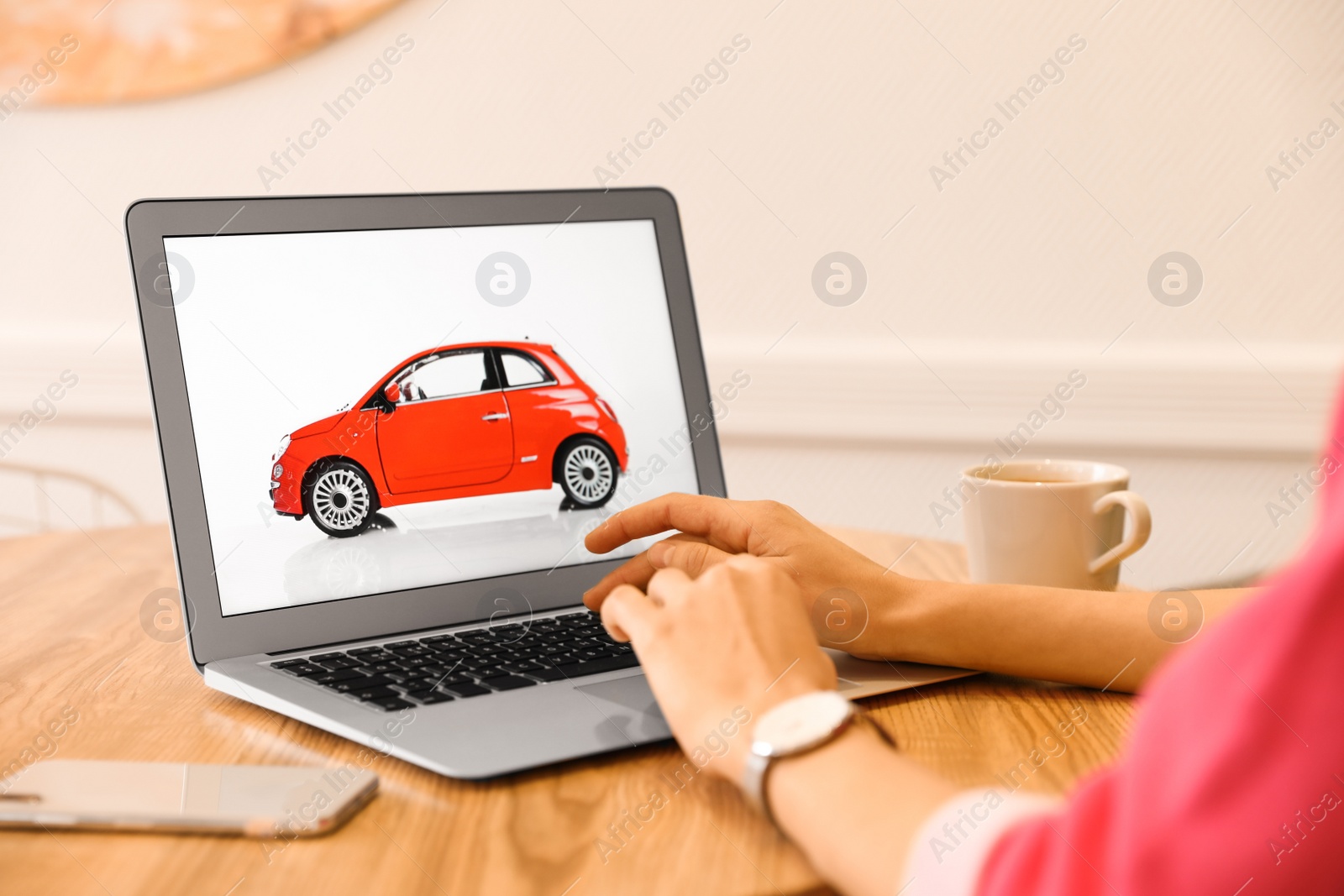 Photo of Woman using laptop to buy car at wooden table indoors, closeup