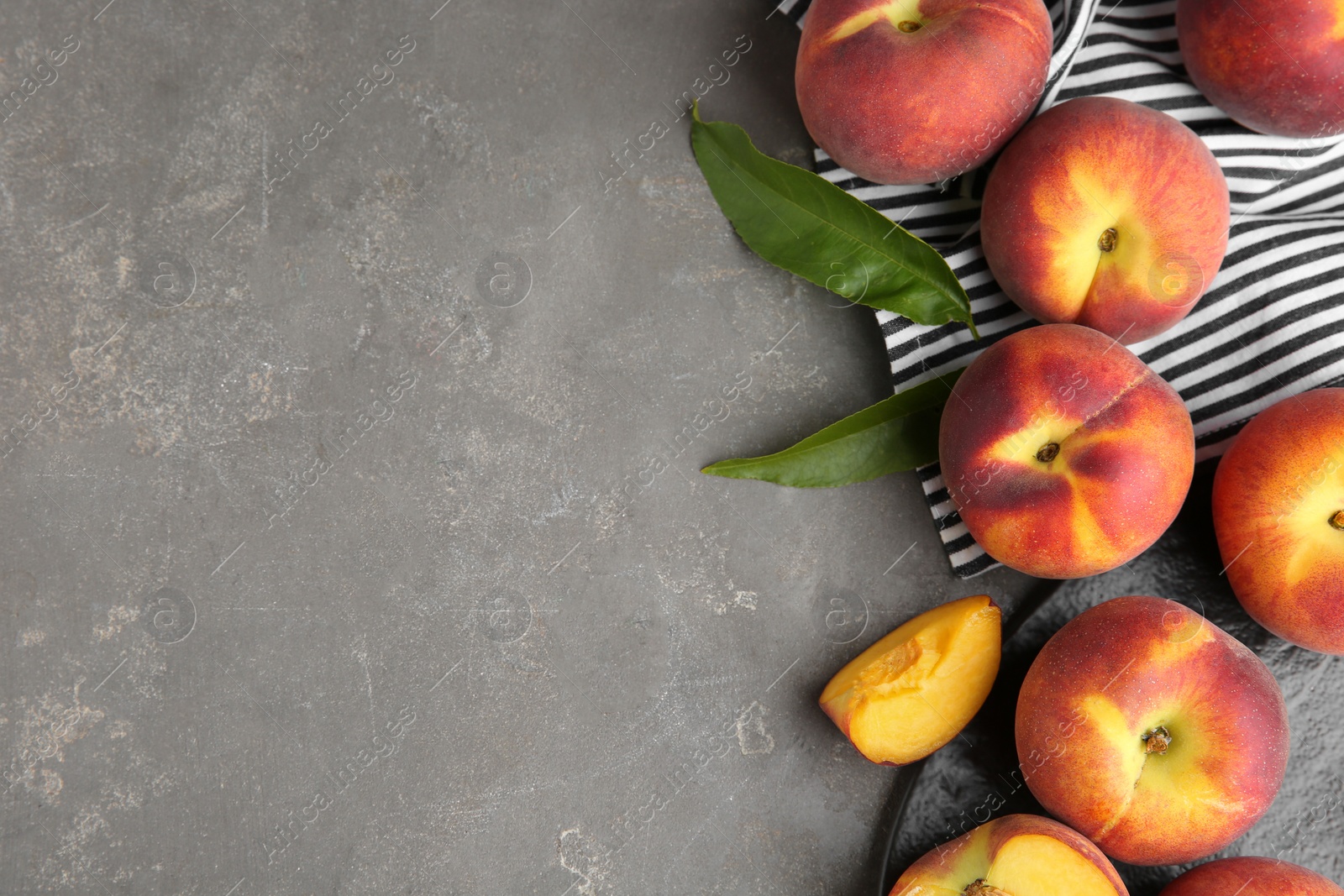 Photo of Fresh tasty peaches, fabric and leaves on grey stone surface, top view with space for text