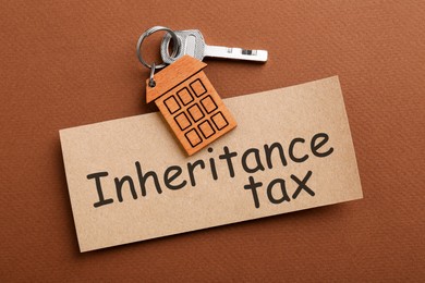 Photo of Card with phrase Inheritance Tax and key with house shaped key chain on brown background, top view