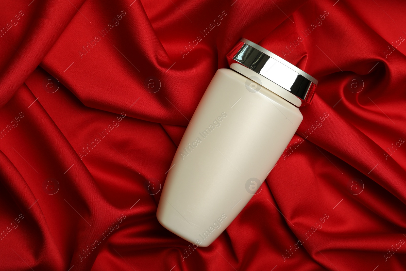 Photo of Bottle of hair care cosmetic product on red fabric, top view