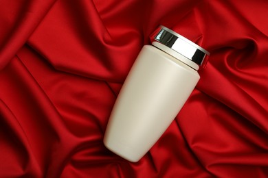 Bottle of hair care cosmetic product on red fabric, top view