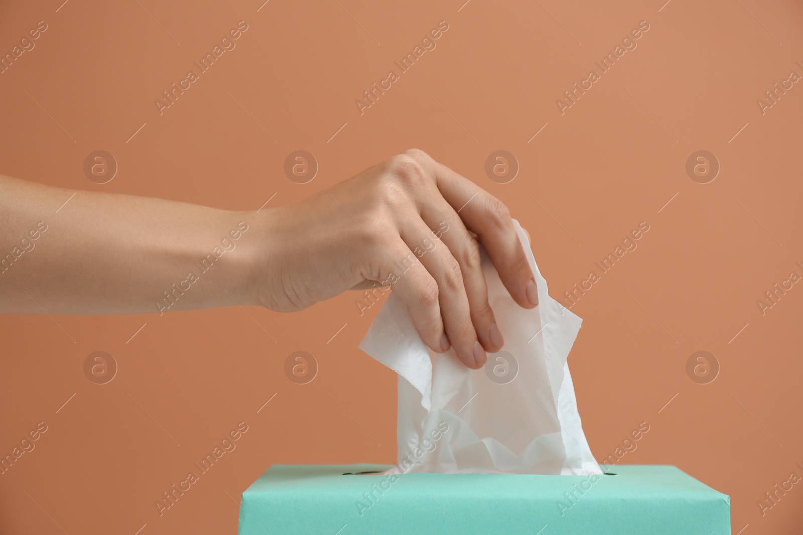 Photo of Woman taking paper tissue from box on light brown background, closeup