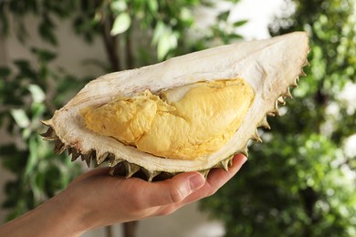 Photo of Woman holding piece of ripe durian on blurred background, closeup