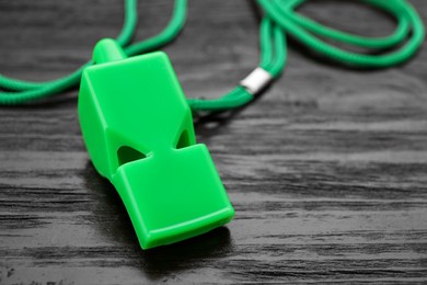 Photo of One green whistle with cord on wooden table, closeup. Space for text