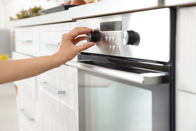 Woman regulating cooking mode on oven panel in kitchen, closeup