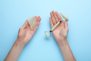 Photo of Woman holding gua sha tool and face roller on light blue background, top view