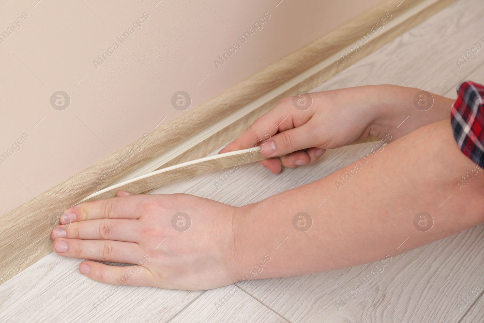 Photo of Man installing plinth on laminated floor in room, closeup