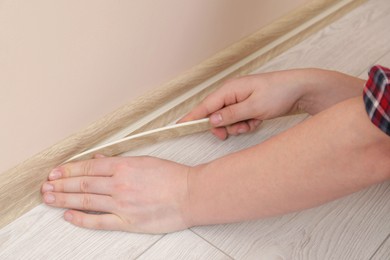 Man installing plinth on laminated floor in room, closeup