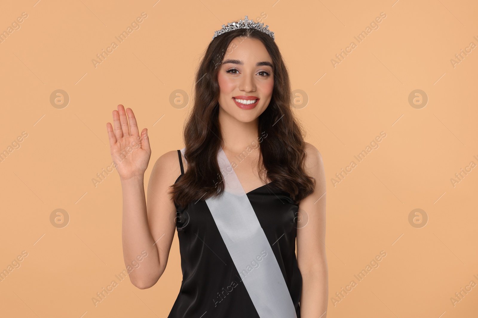 Photo of Beautiful young woman with tiara and ribbon in dress on beige background. Beauty contest