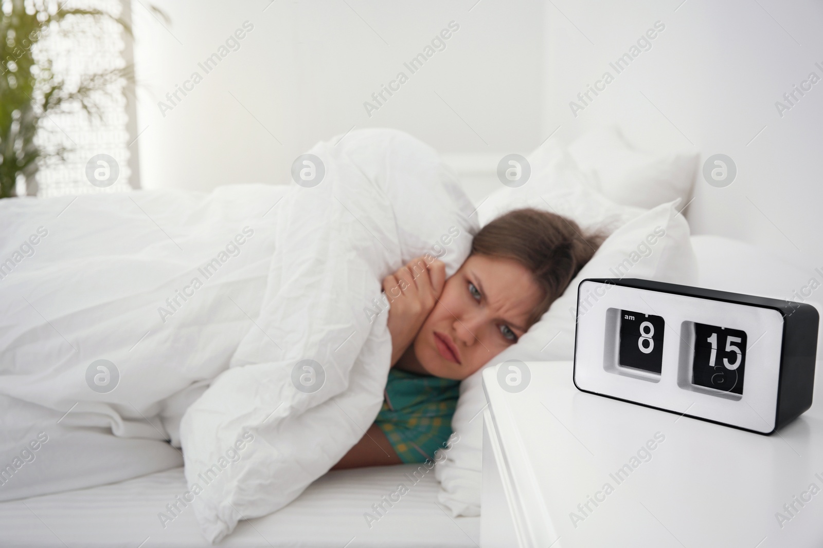 Photo of Young woman covering herself at home in morning, focus on clock