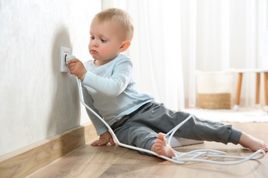 Photo of Little child playing with electrical socket and plug at home. Dangerous situation