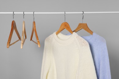 Photo of Rack with warm sweaters and hangers on light grey background