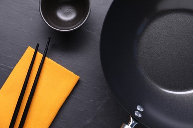 Empty iron wok, sauce bowl and chopsticks on black table, flat lay