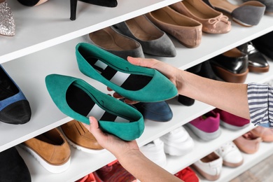 Photo of Woman taking shoes from shelving unit, closeup