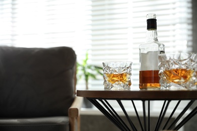 Glasses and bottle of whiskey on table indoors. Space for text