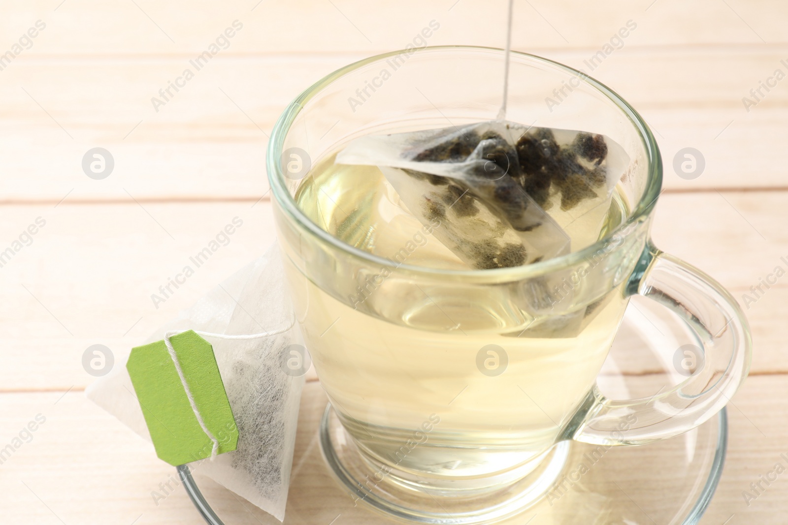 Photo of Putting tea bag in glass cup on light wooden table, closeup