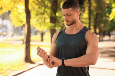 Photo of Attractive serious man checking pulse after training in park on sunny day. Space for text