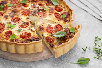 Photo of Cut delicious homemade quiche with prosciutto on light grey table, closeup