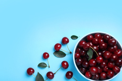 Photo of Sweet juicy cherries with leaves on light blue background, flat lay. Space for text