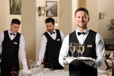 Photo of Butler holding tray with glasses of sparkling wine in restaurant. Space for text