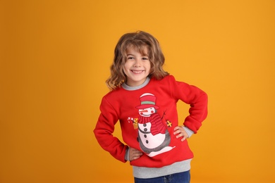 Photo of Cute little girl in red Christmas sweater smiling against orange background
