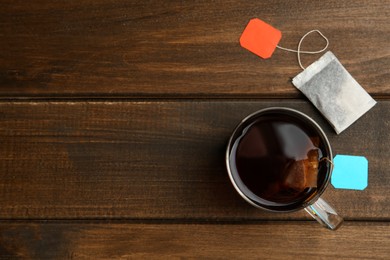 Photo of Tea bags in glass cup of hot water on wooden table, flat lay. Space for text