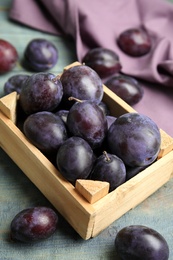 Delicious ripe plums in crate on blue wooden table