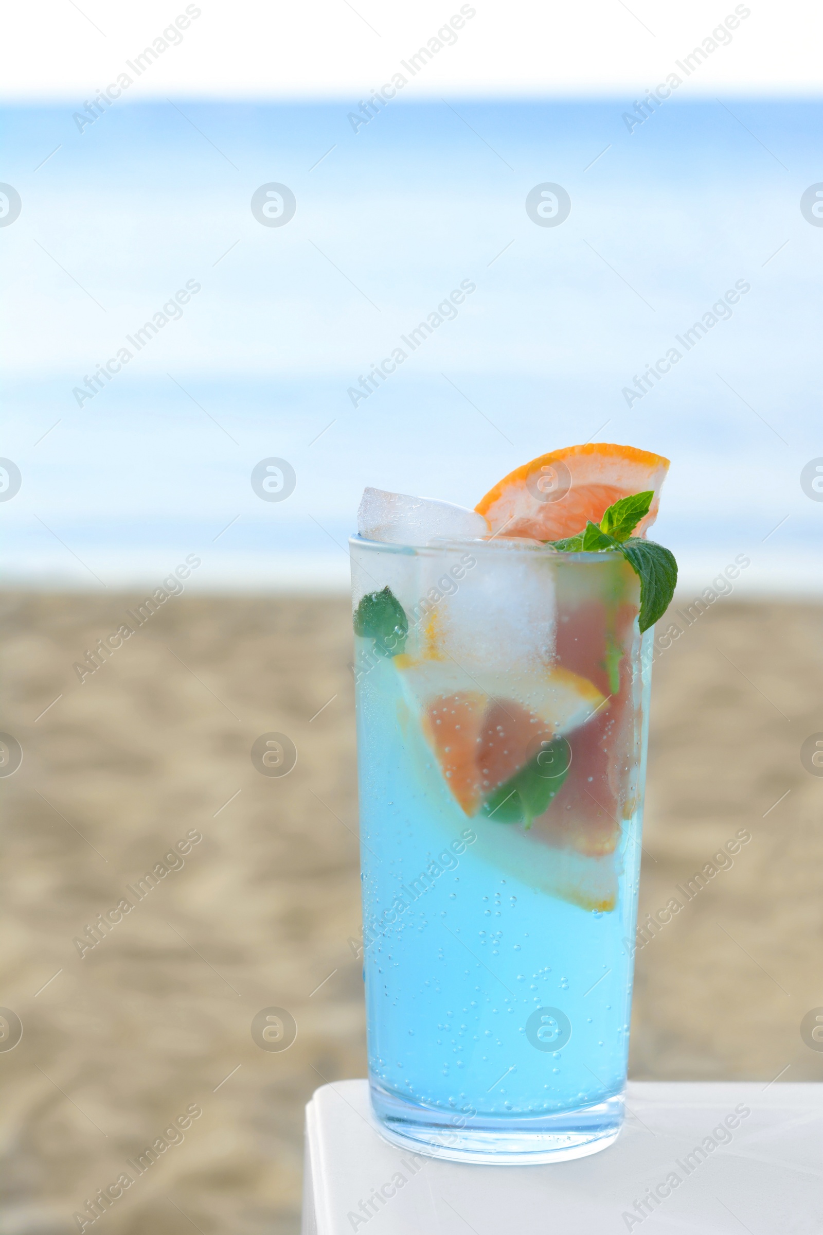 Photo of Glass of refreshing drink with grapefruit and mint on white table near sea