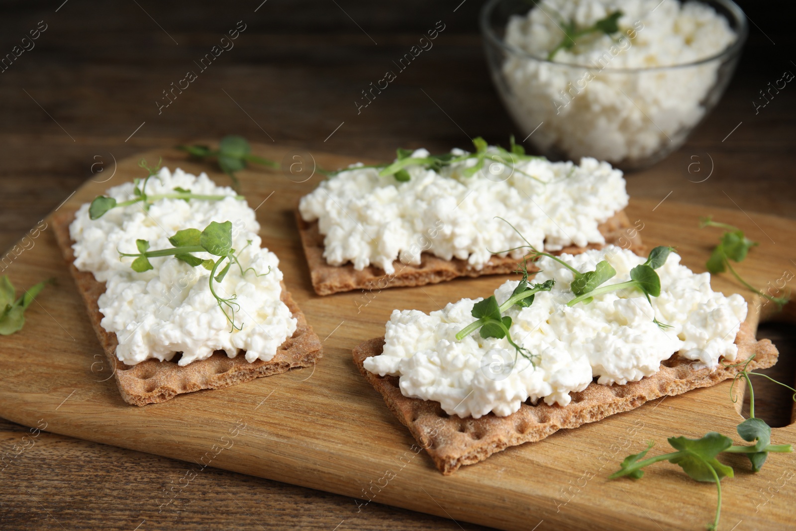 Photo of Crispy crackers with cottage cheese and microgreens on wooden table, closeup