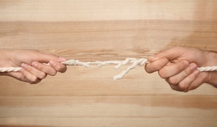 Photo of Man and woman pulling frayed rope at breaking point on wooden background