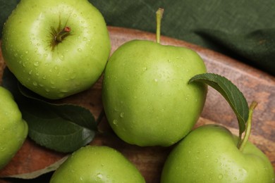 Photo of Ripe green apples with leaves and water drops on wooden board, top view