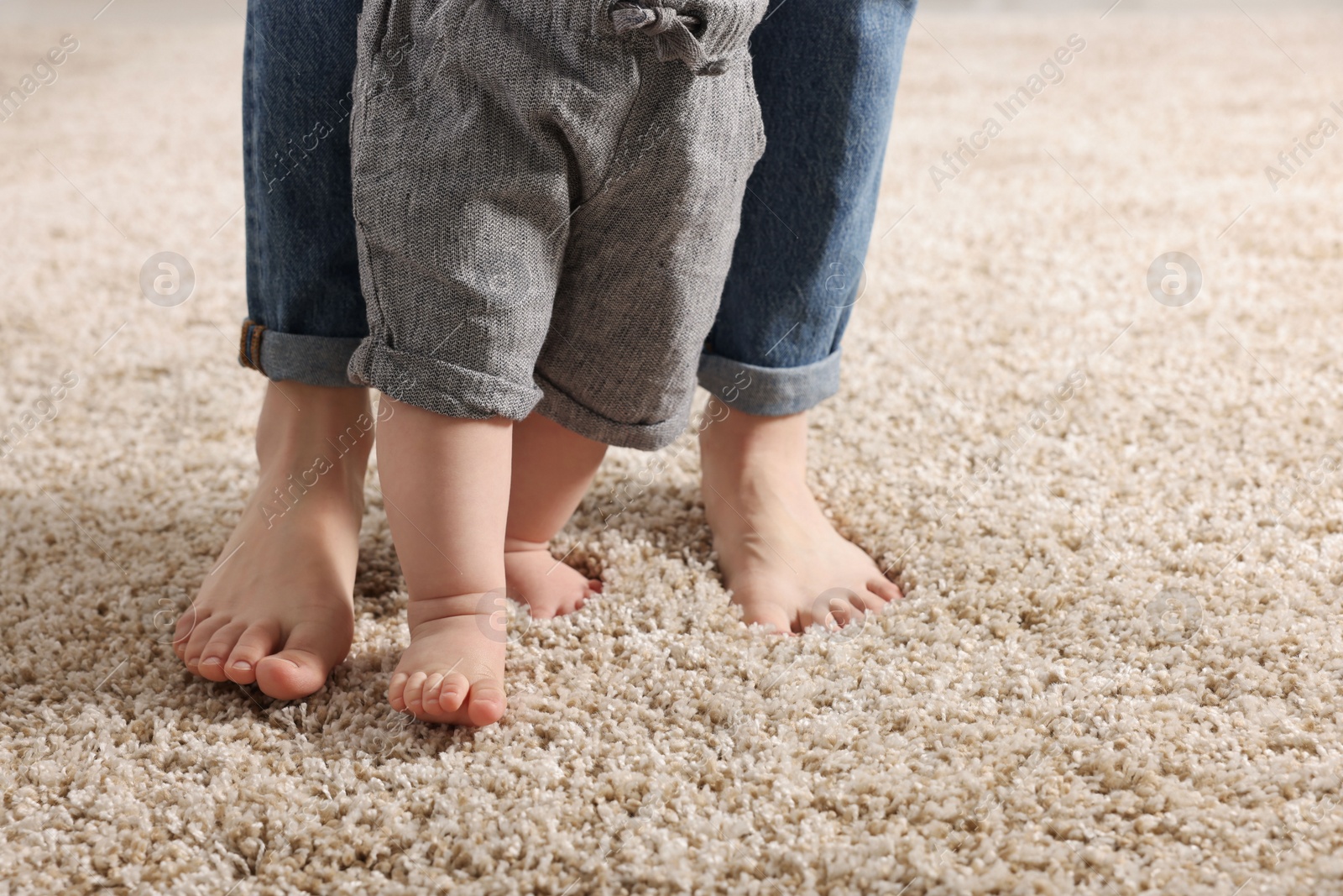 Photo of Mother supporting her baby son while he learning to walk on carpet, closeup