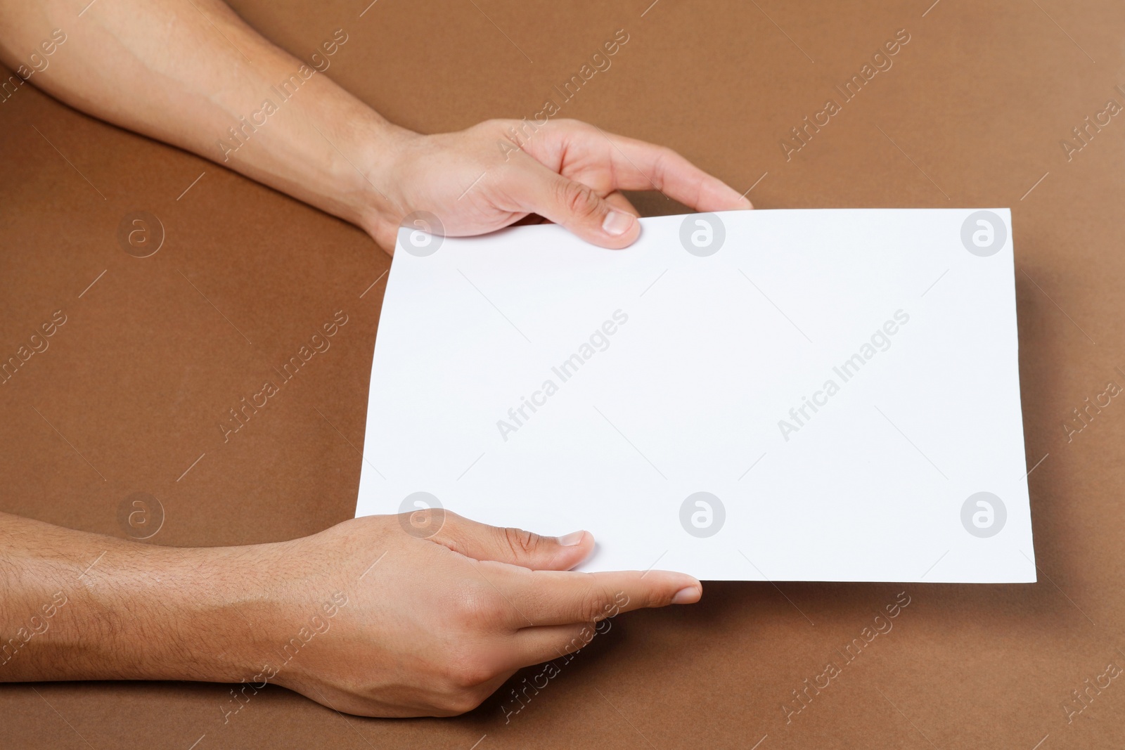 Photo of Man holding sheet of paper on brown background, closeup. Mockup for design