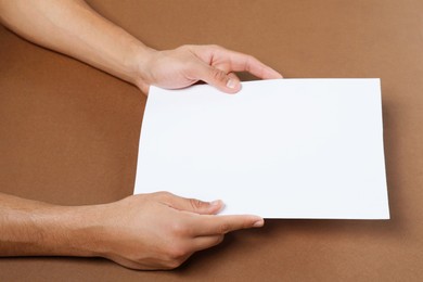 Photo of Man holding sheet of paper on brown background, closeup. Mockup for design