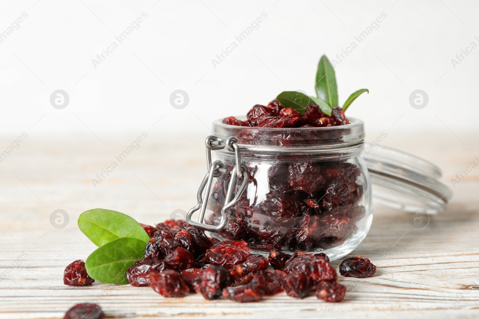 Photo of Tasty dried cranberries and leaves on white wooden table