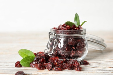 Tasty dried cranberries and leaves on white wooden table