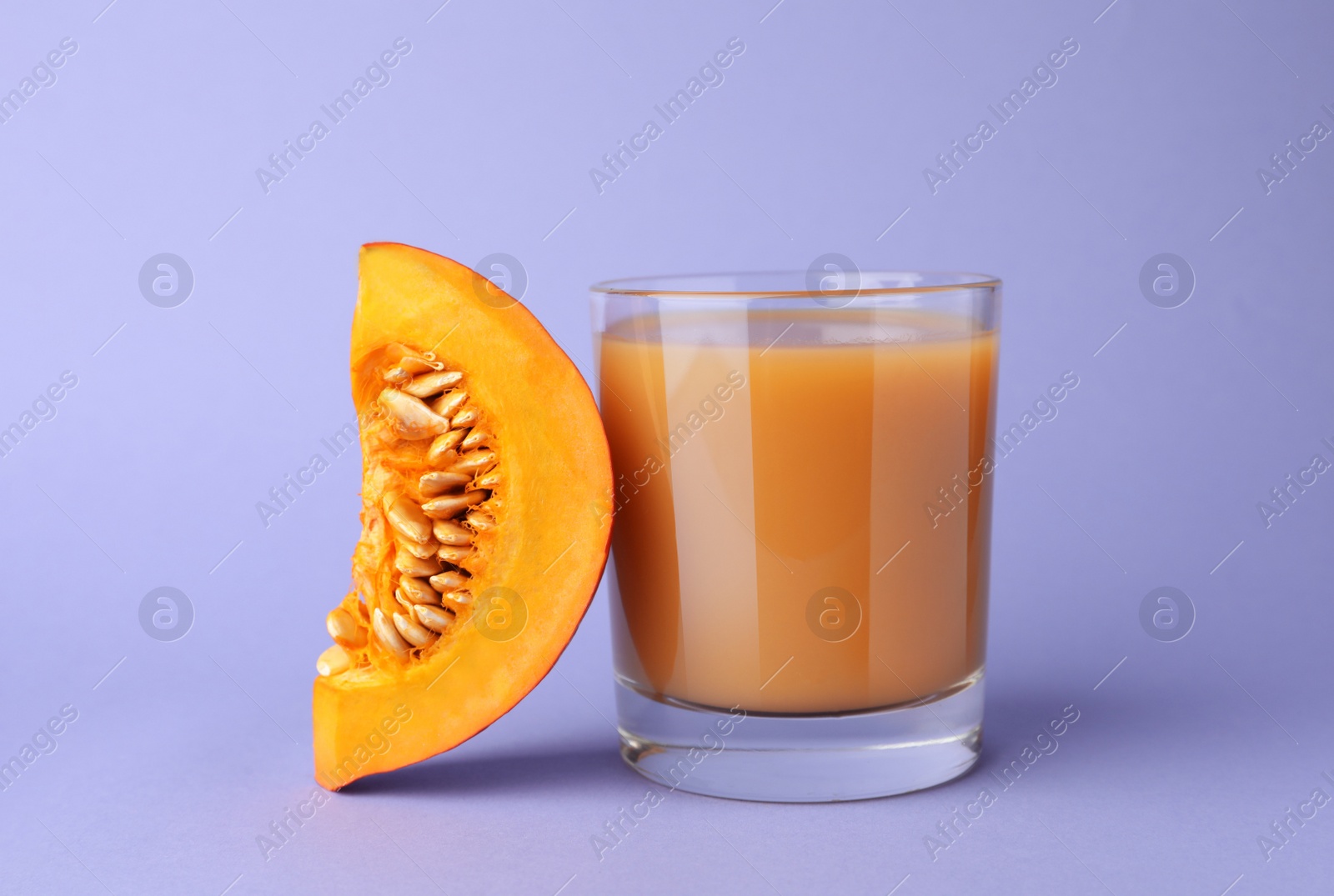 Photo of Tasty pumpkin juice in glass and cut pumpkin on lavender color background