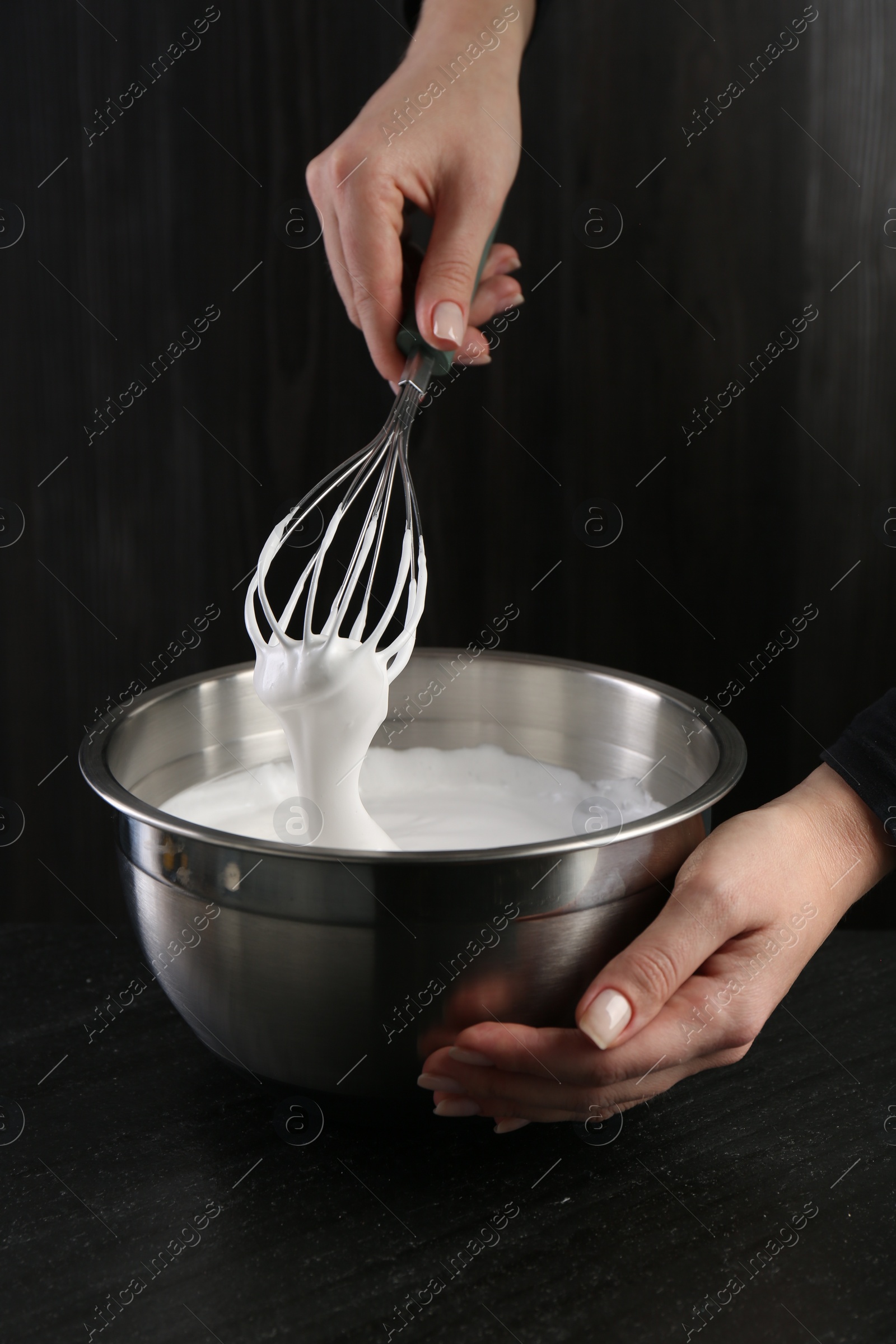 Photo of Woman making whipped cream with whisk at black table, closeup